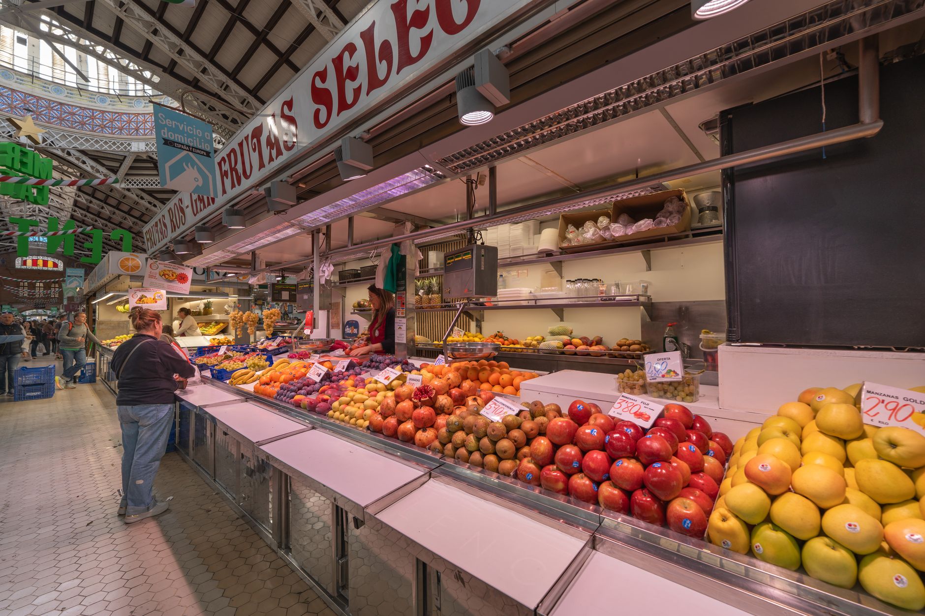 A fruit counter piled with apples, pomegranates and citrus inside a covered market hall